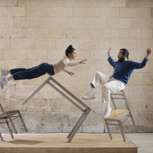 Deux artistes circassiens performant sur un dispositif dit "la table et les chaises" et jouant avec la notion de déséquilibre.